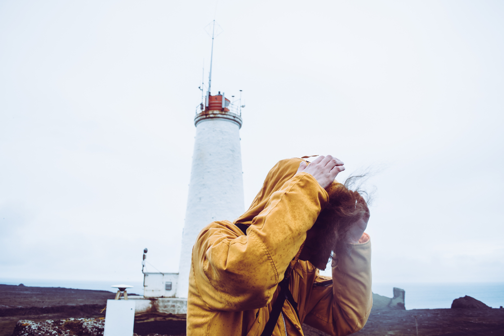 Iceland stormy weather. Traveler fighting a storm in Iceland near a lighthouse.