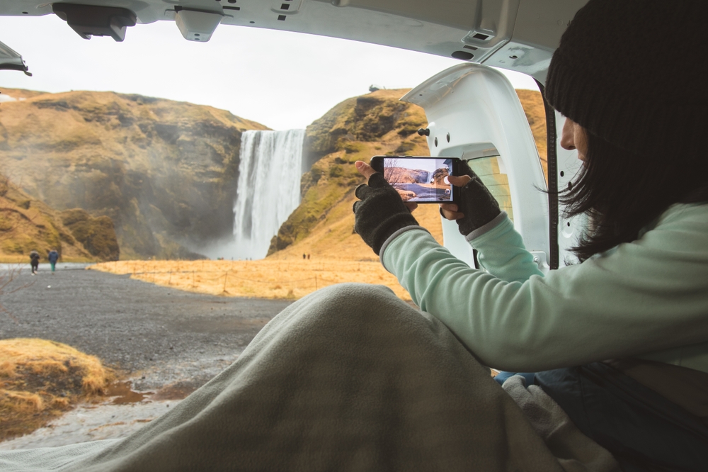 Skogafoss waterfall camper van. Women sitting in a camper van taking a photo of Skogafoss waterfall.
