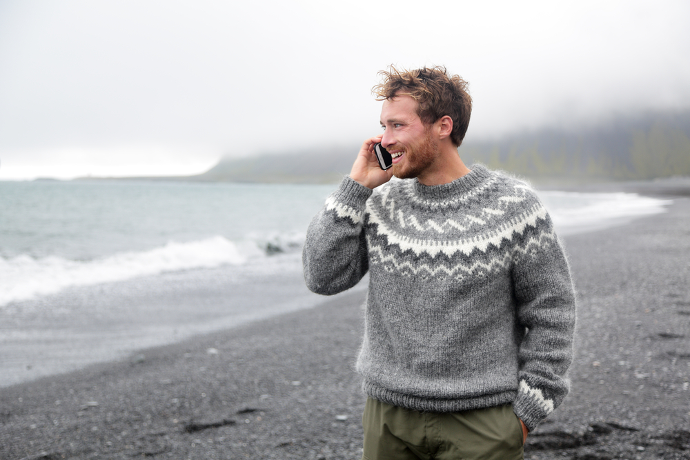 Stay connected in Iceland. Man in wool sweater on his phone on Iceland black sand beach.