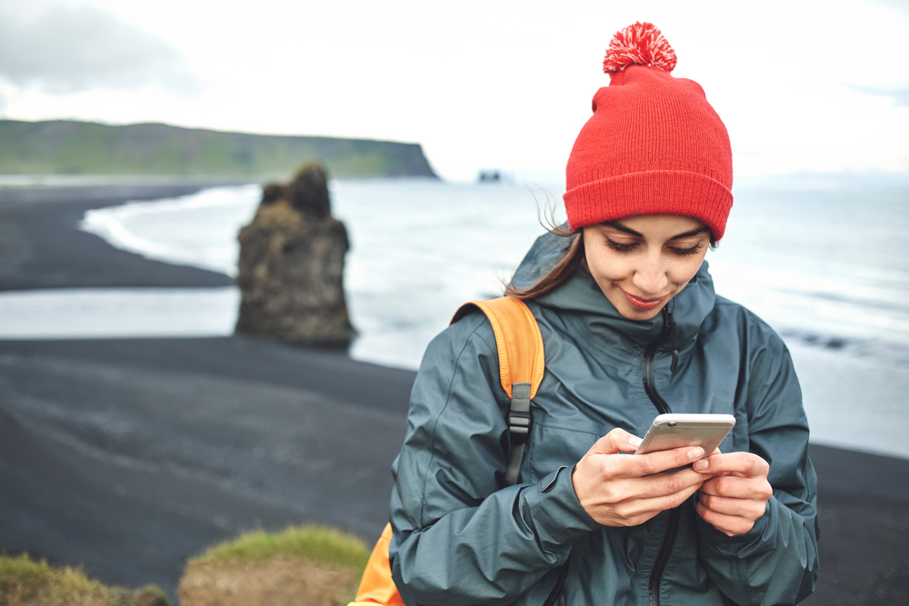 Dyrhólaey and Reynisfjara. Women using a smart phone at Dyrhólaey with Reynisfjara in the background.