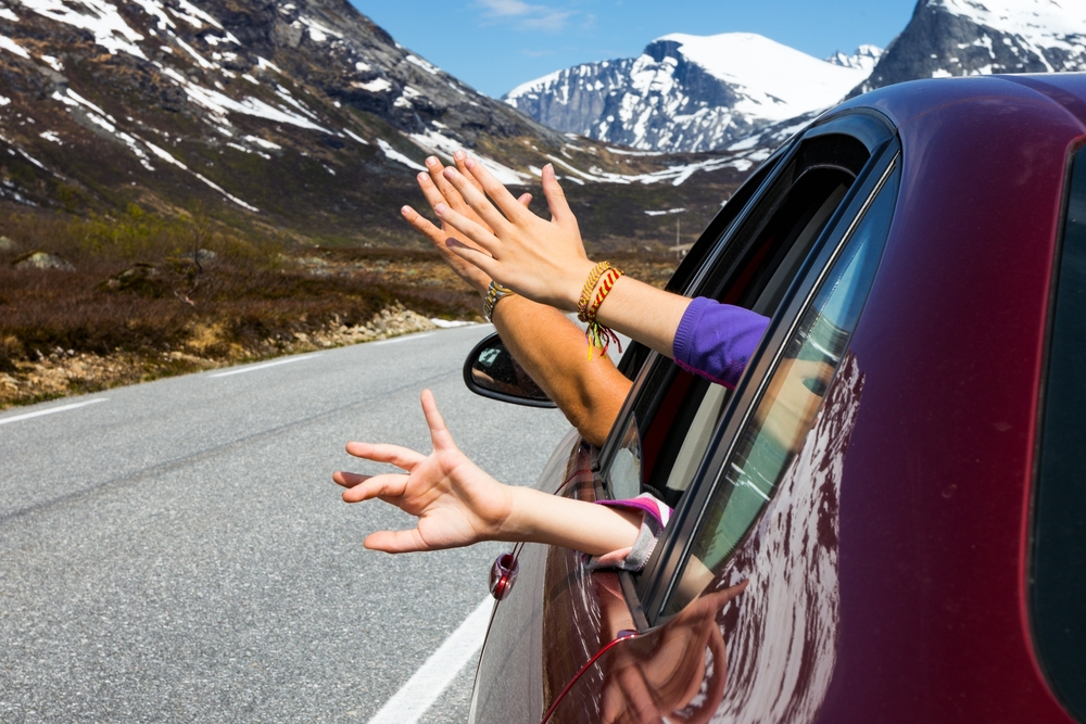 Iceland family rental car. Family in a rental car in Iceland waving with mountain view.