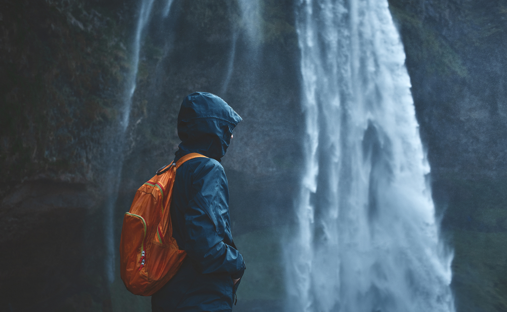 Waterproof outwear. Person in waterproof outwear standing in front of a waterfall in Iceland.