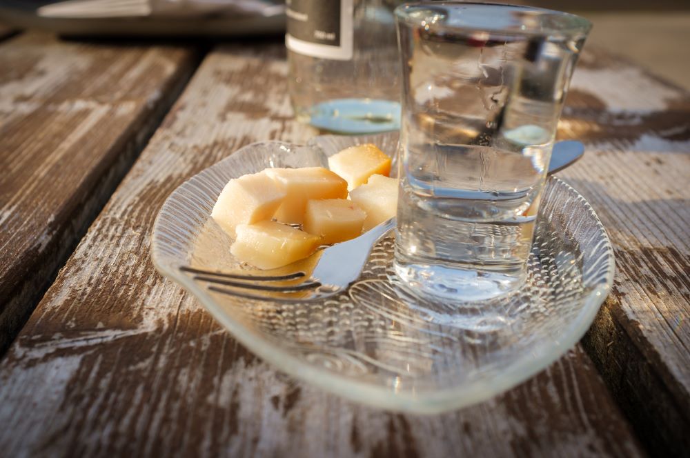 A shot of Brennivín and a bites of fermented shark on a plate. 